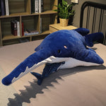 Peluche Requin-Scie bleu sur un lit avec une peluche requin-baleine dans sa bouche